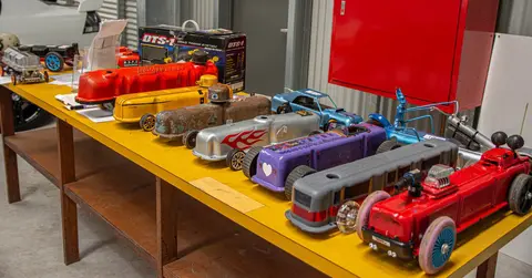 A collection of handmade toy cars on a yellow table indoors.