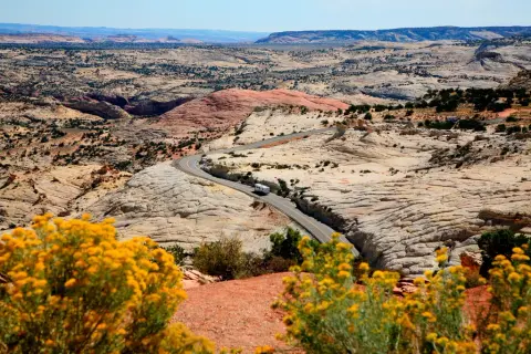A winding road cuts through a vast desert landscape with rocky terrain and sparse vegetation.