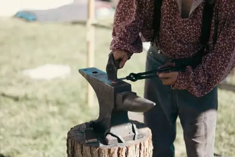 A person working at an anvil outdoors.