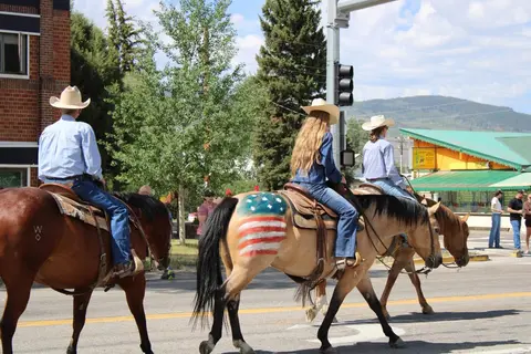 Three people ride horses down a street in a parade.