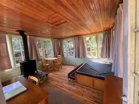 An interior view of a rustic wooden cabin with a wood stove and bed.
