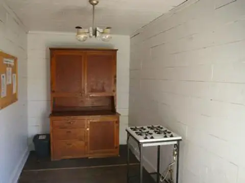 An interior view of a room with white block walls, a wooden cabinet, and a small stove.