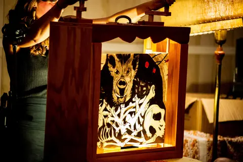 A person operates a wooden crank device displaying an illuminated illustration of an animal and bones.