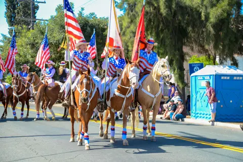 A group of people ride horses carrying flags in a parade.