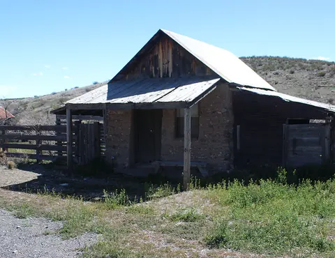 An old rustic building with a porch stands in a dry landscape.