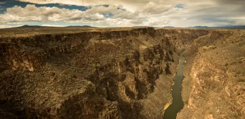 A wide canyon with a river flowing through the bottom under a cloudy sky.