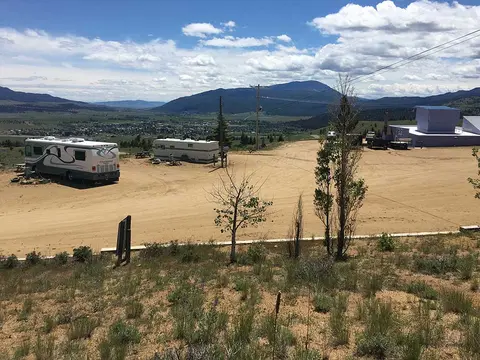 An elevated view of a dirt area with parked RVs overlooking a valley and distant mountains.
