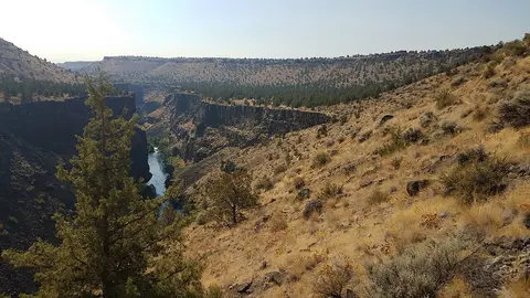 A river runs through a rocky canyon landscape with sparse vegetation.