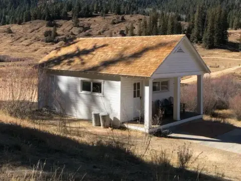 A small white building with a wooden porch and roof stands in a rural landscape.