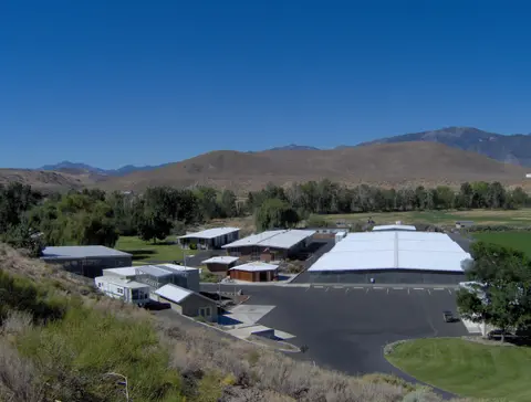 An elevated view of a complex of buildings in a valley with mountains in the background.