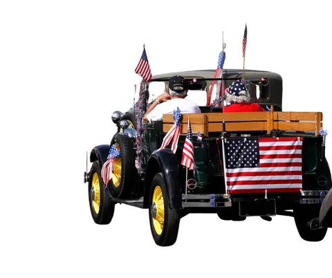 A vintage truck decorated with American flags is driven by two people.