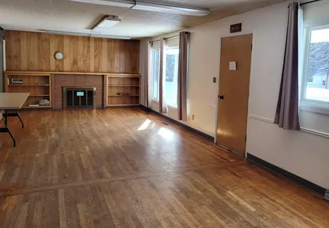 An empty room with a wooden floor, fireplace, and large windows.