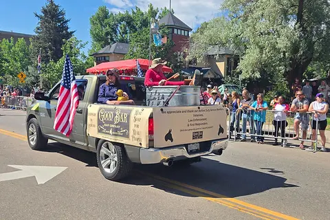 A decorated pickup truck drives down a street in a parade as spectators watch from the sidelines.