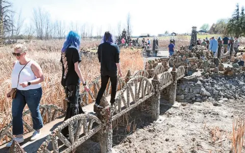 People walk across a decorative concrete bridge outdoors.