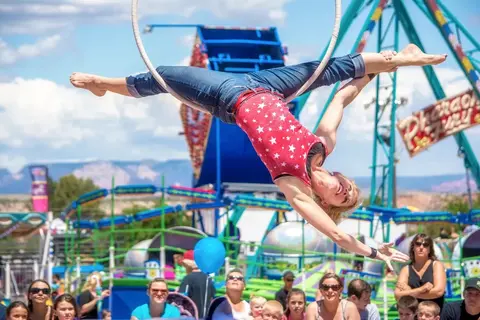 A performer does aerial acrobatics on a ring at an outdoor carnival.