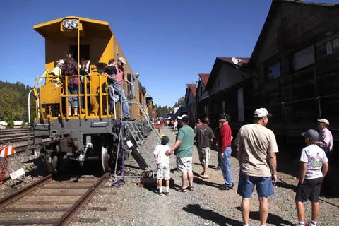 People boarding a yellow train car next to a wooden building.