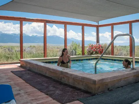 Two women soak in an outdoor hot tub with mountain views in the distance.