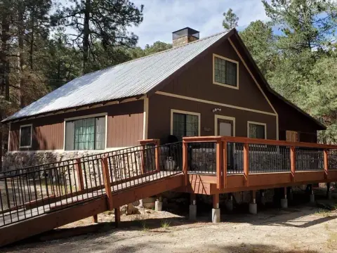 Exterior view of a cabin with a wooden deck and ramp among trees.