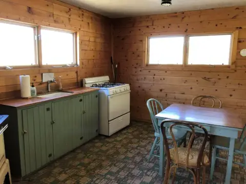 An interior view of a rustic kitchen with wooden paneled walls, a green cabinet, and a dining table.