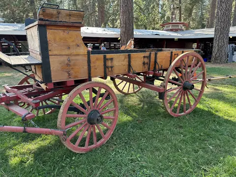 An old wooden wagon with red wheels sits on grass outdoors.
