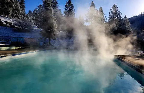 A steaming outdoor swimming pool surrounded by snow-covered trees.