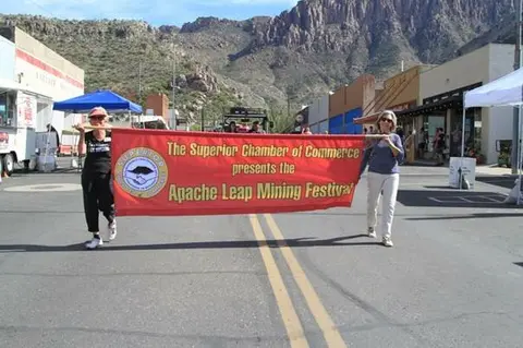Two women carry a banner presenting a festival down a street.
