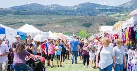 A crowd of people walking among vendor tents at an outdoor market with mountains in the background.