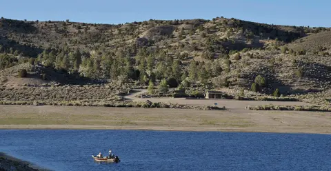 A boat on a lake in front of hills and trees.