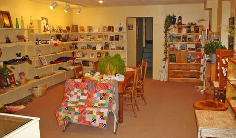 An interior view of a shop with shelves of books and crafts, and a table in the center.