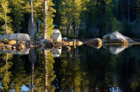 Trees and rocks are reflected in a calm lake.