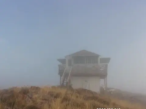 A fire lookout tower stands on a misty mountain ridge.