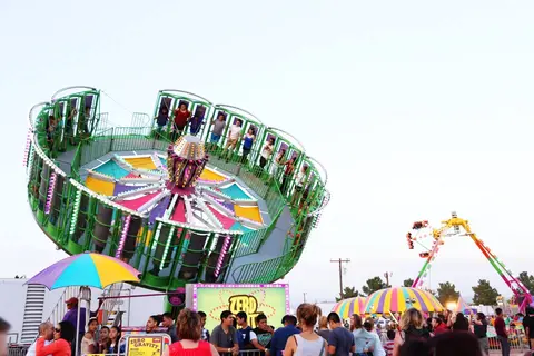 People enjoy a large spinning ride at an outdoor carnival.