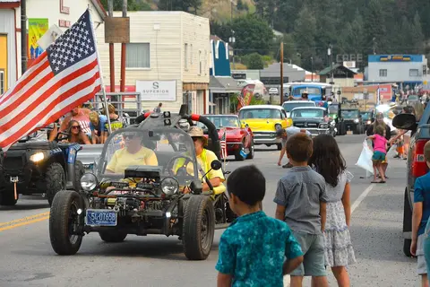A street parade with vehicles and onlookers.