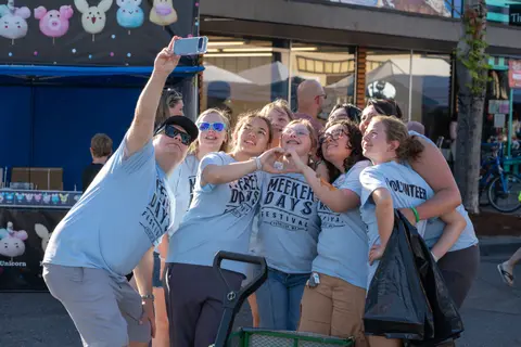 A group of people in matching t-shirts take a selfie together outdoors at a festival.