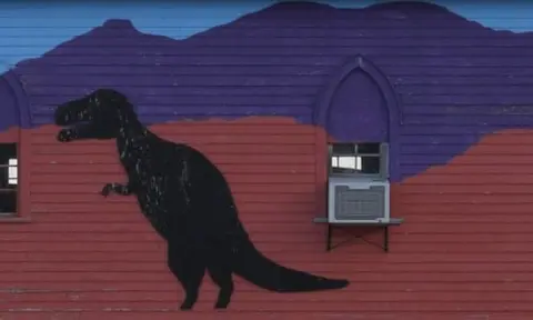A painted exterior wall features a large silhouette of a dinosaur and a mural of mountains.