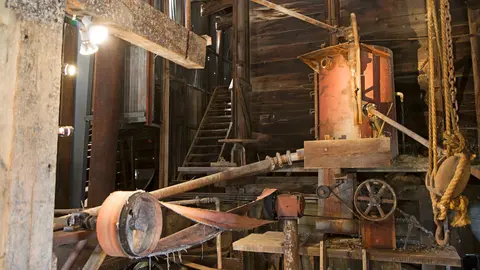 The interior of a rustic industrial building featuring vintage machinery and wooden structures.