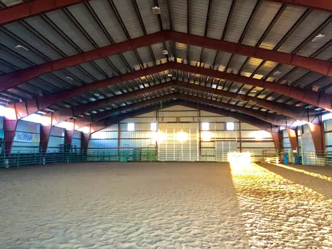 An indoor riding arena with a sand floor and exposed metal framing.