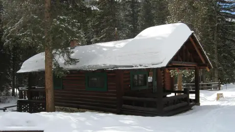 A log cabin covered in snow in a snowy forest.