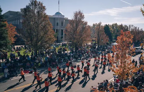 A marching band performs in a street parade past a large crowd.