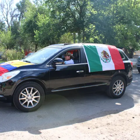 A black SUV decorated with flags drives down a paved road.