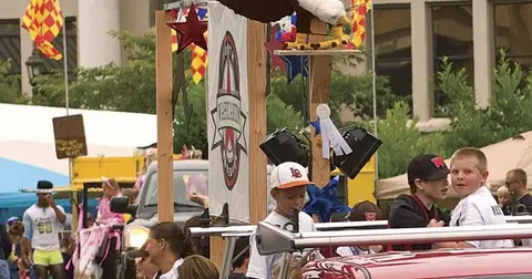 A parade float with a wooden structure, a large eagle, and banners, surrounded by people.