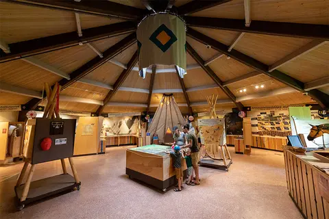 A family visits a museum with exhibits inside a round wooden building.