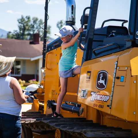 A child climbs onto a large yellow tractor while an adult watches.