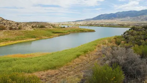 A river flows through a landscape with hills and distant mountains under a cloudy sky.