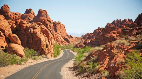A winding road passes through a desert landscape with red rock formations.