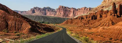A paved road winding through a desert landscape with red rock formations and mountains.