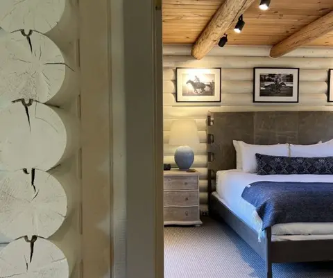 An interior view of a bedroom with log walls and a bed, seen through a doorway.