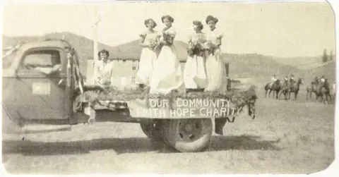 Historic photo showing people on a decorated truck float in a parade.