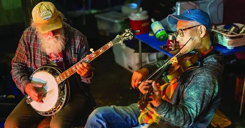Two men play a banjo and a fiddle outdoors.