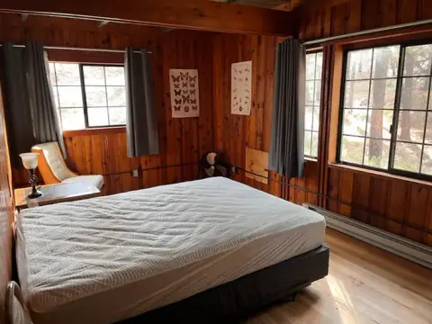 A bedroom with wood-paneled walls and windows looking outside.